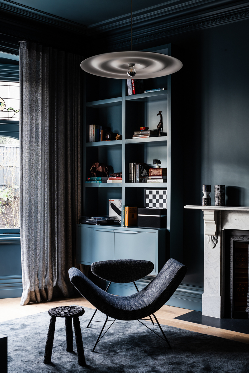 Reading nook with deep blue walls, boucle lounge chair, layered dark curtains, and statement pendant lighting.